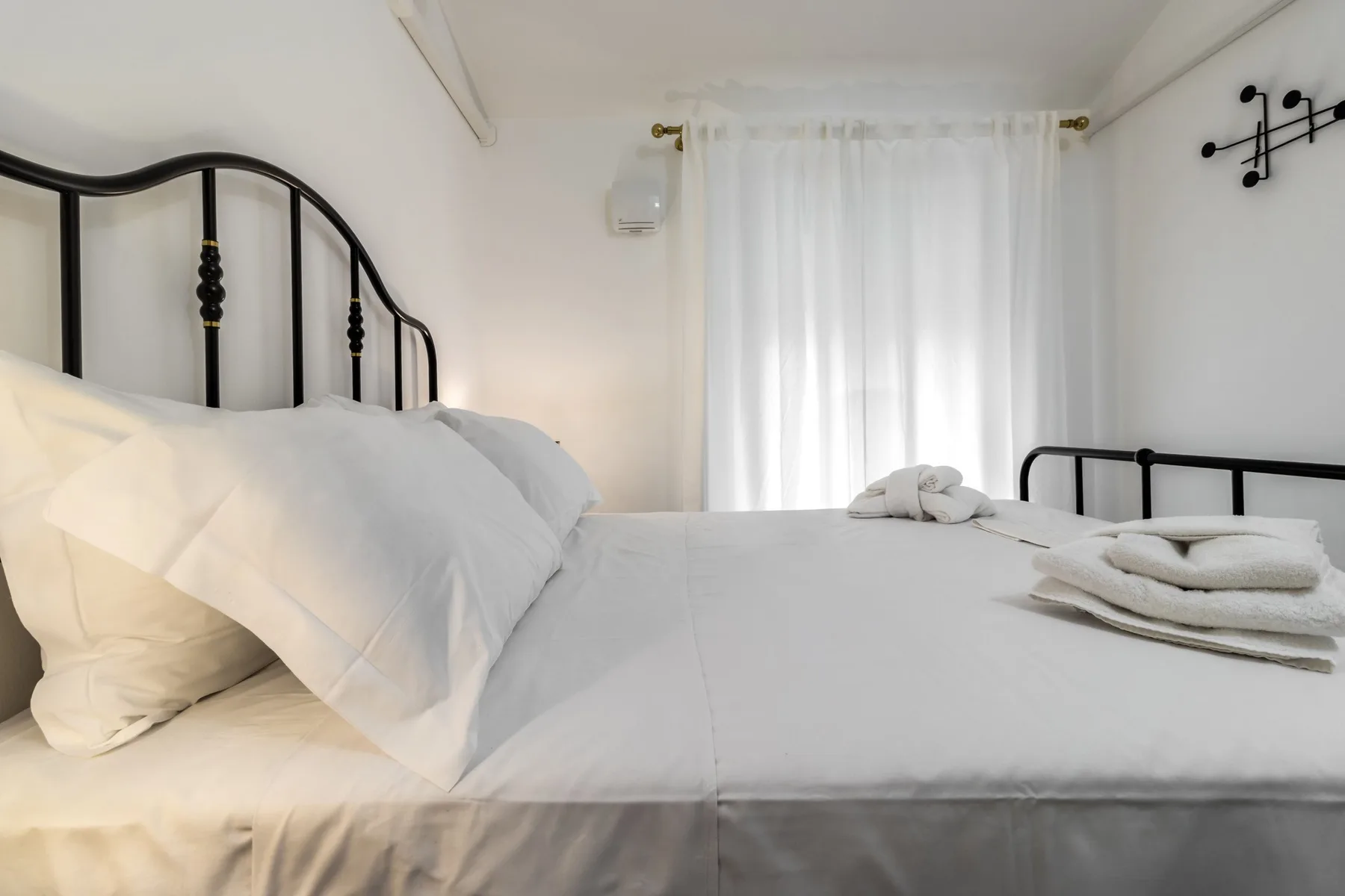 A bedroom with a neatly made bed and a bright curtained window.