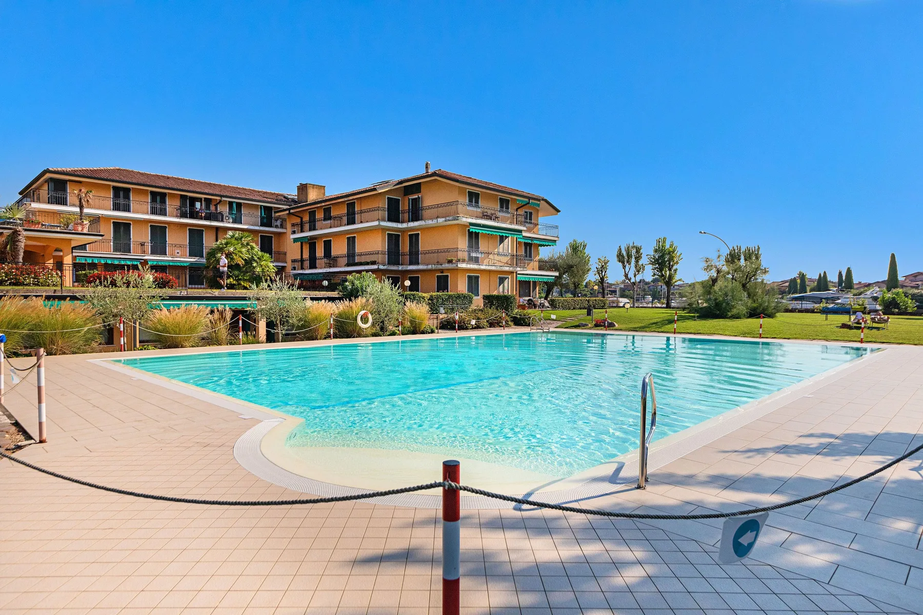 An outdoor swimming pool sits beside a multi-story building under a clear blue sky.