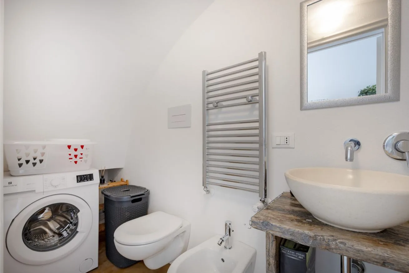 A bright bathroom with a washing machine, wall-mounted towel warmer, and sink.