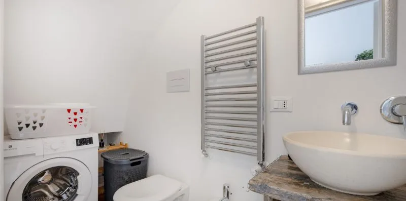 A bathroom with a washing machine, towel radiator, and sink.