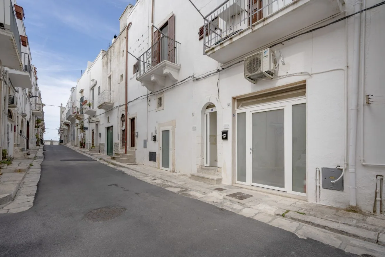 A narrow street runs between white buildings with balconies and storefront doors.