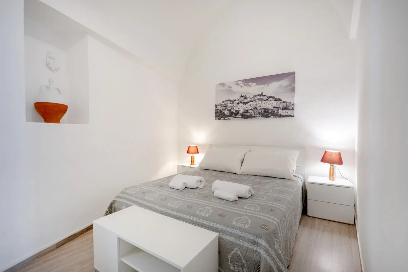 A bright bedroom with a neatly made bed, bedside tables, and a framed wall picture.