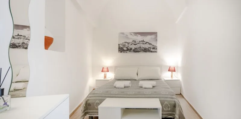 A bright bedroom with a bed, bedside tables, and framed artwork.