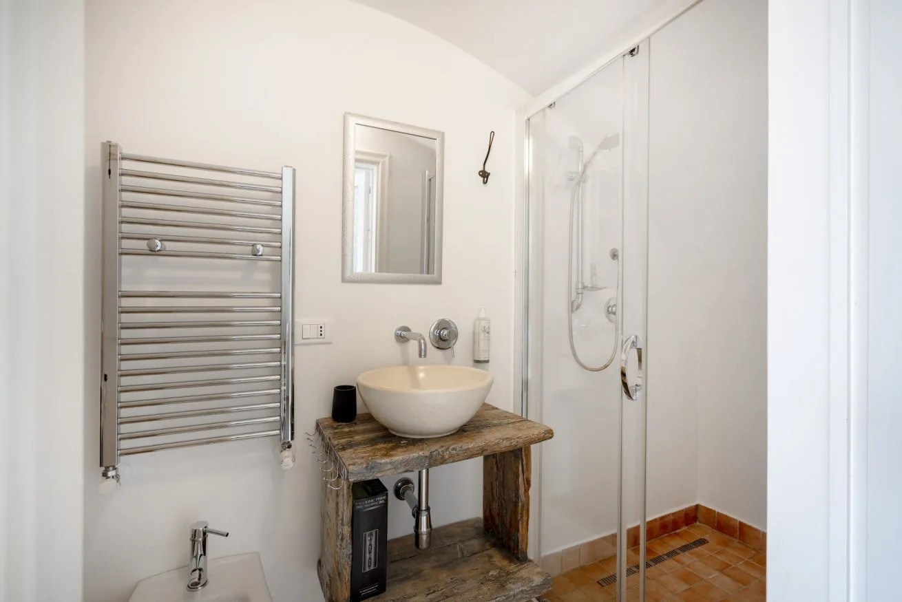 A bathroom with a vessel sink, wall-mounted towel warmer, and glass shower.