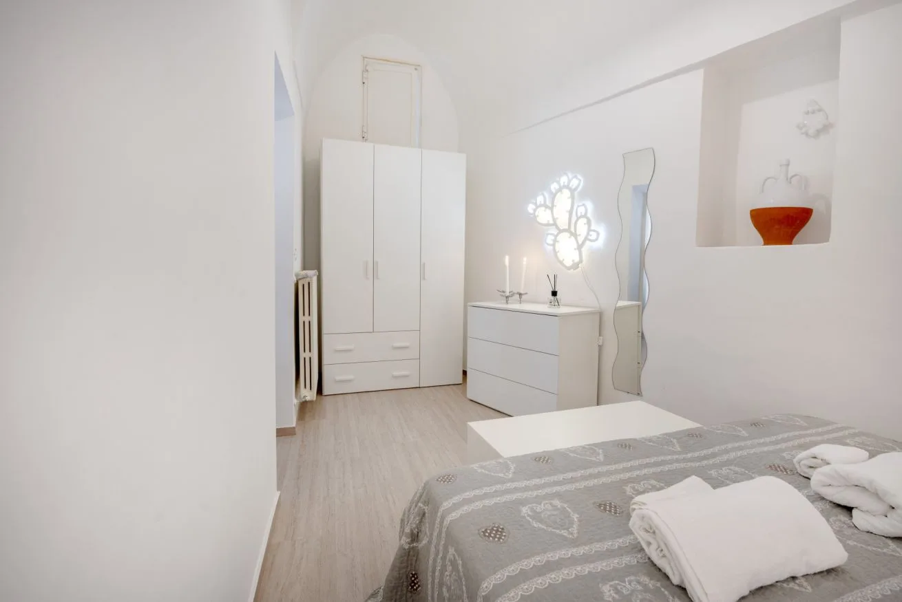 A bright bedroom with a patterned bedspread and white storage furniture.