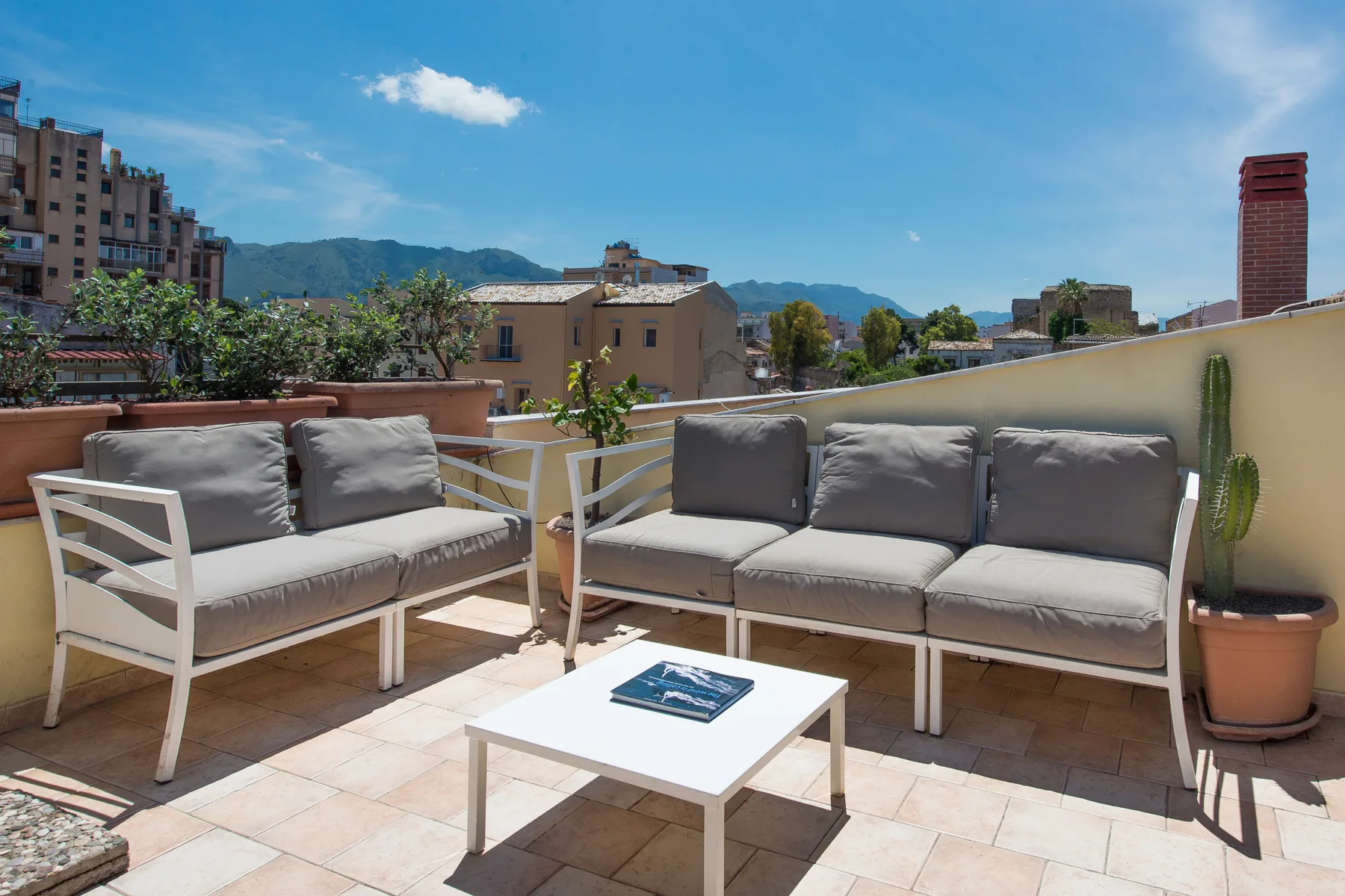 Una terraza en la azotea con asientos acolchados y vistas a edificios y colinas cercanos.