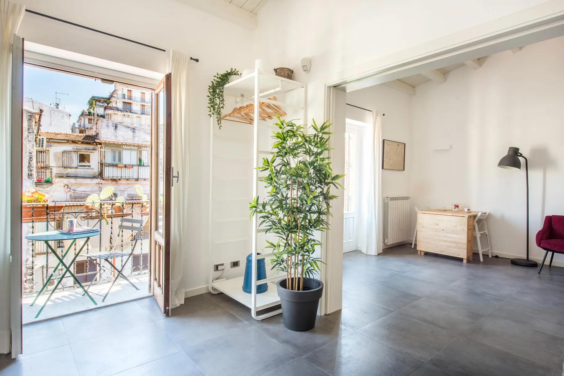 Una habitación luminosa con una planta en maceta y un balcón visible por las puertas abiertas.