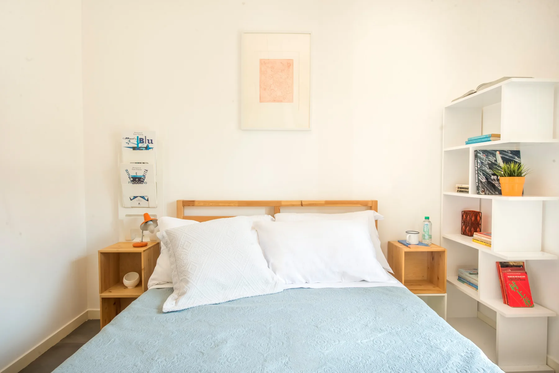 Un dormitorio luminoso con una cama tendida y estanterías abiertas.