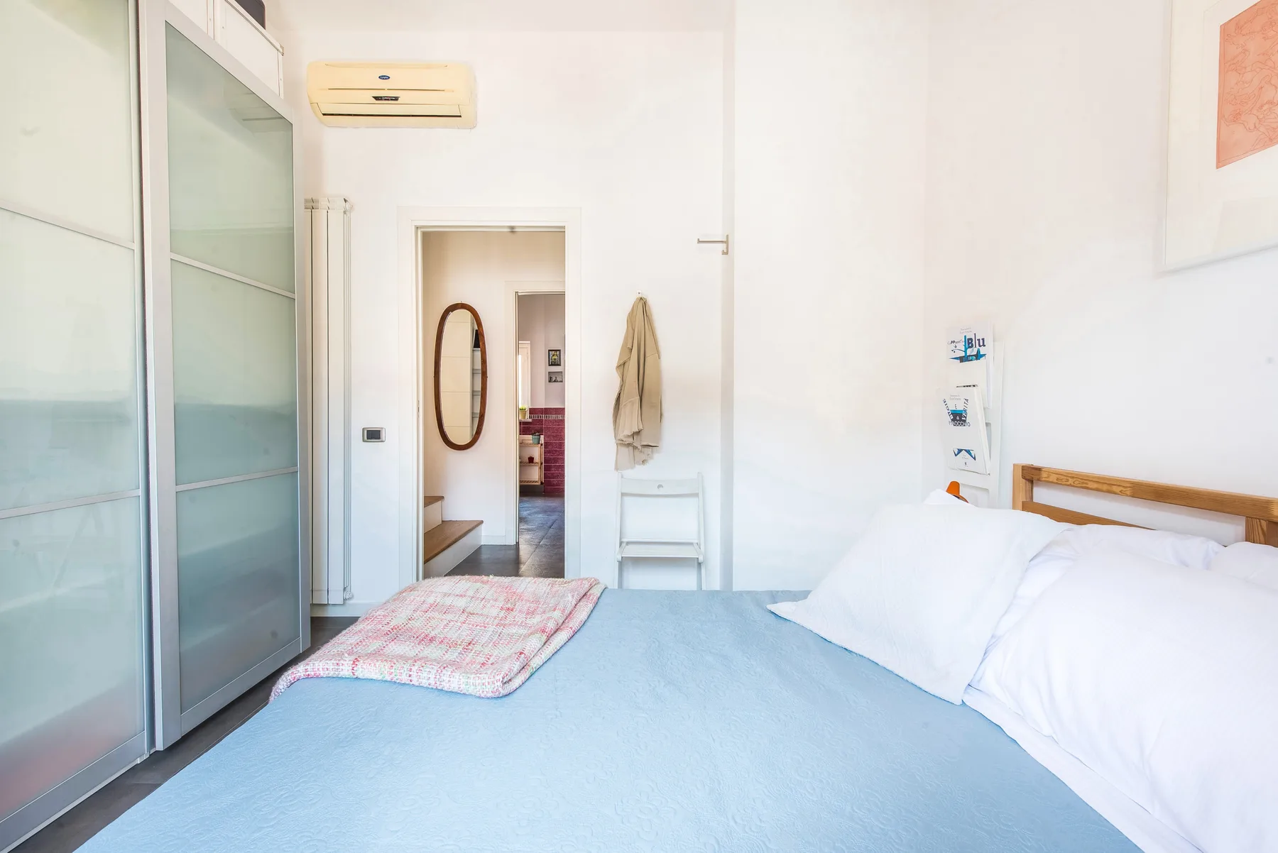 Un dormitorio con una cama, almohadas blancas y un armario corredizo.