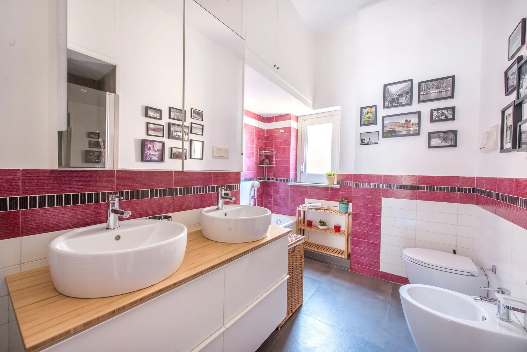 Un baño luminoso con un mueble de lavabo alargado, espejo y detalles de azulejos rojos.