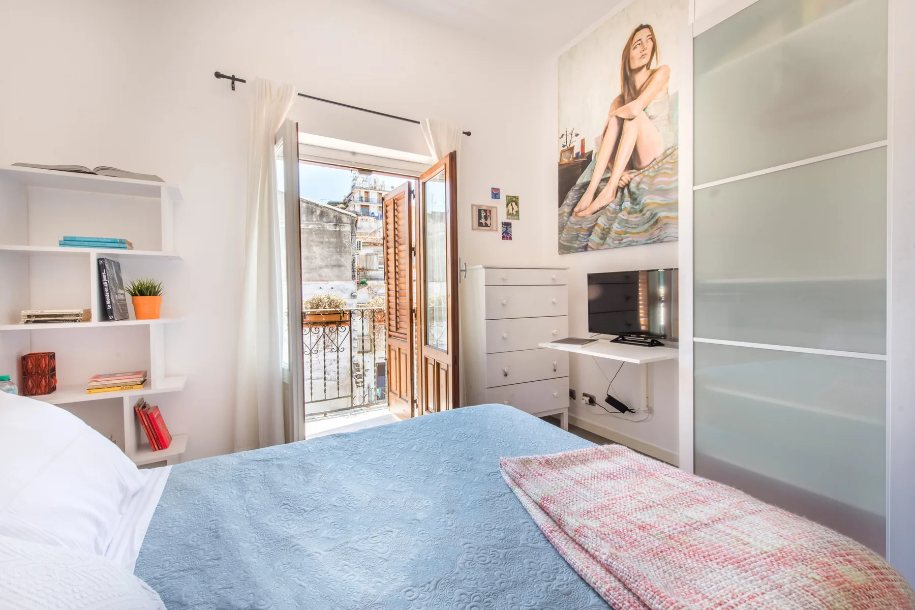 Un dormitorio luminoso con una cama, un televisor y una puerta abierta al balcón.