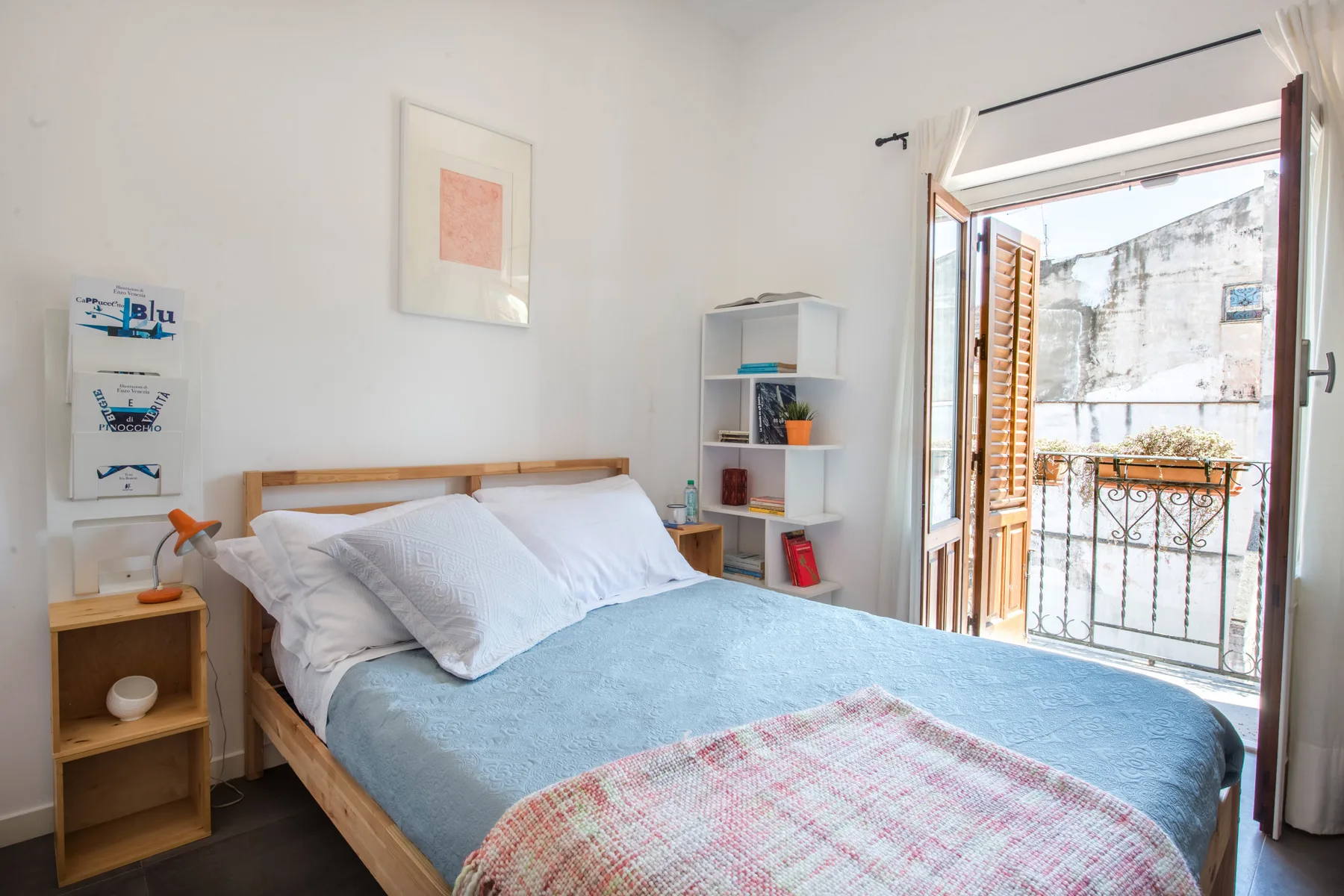 Un dormitorio con una cama de madera, ropa de cama azul claro y la puerta del balcón abierta.