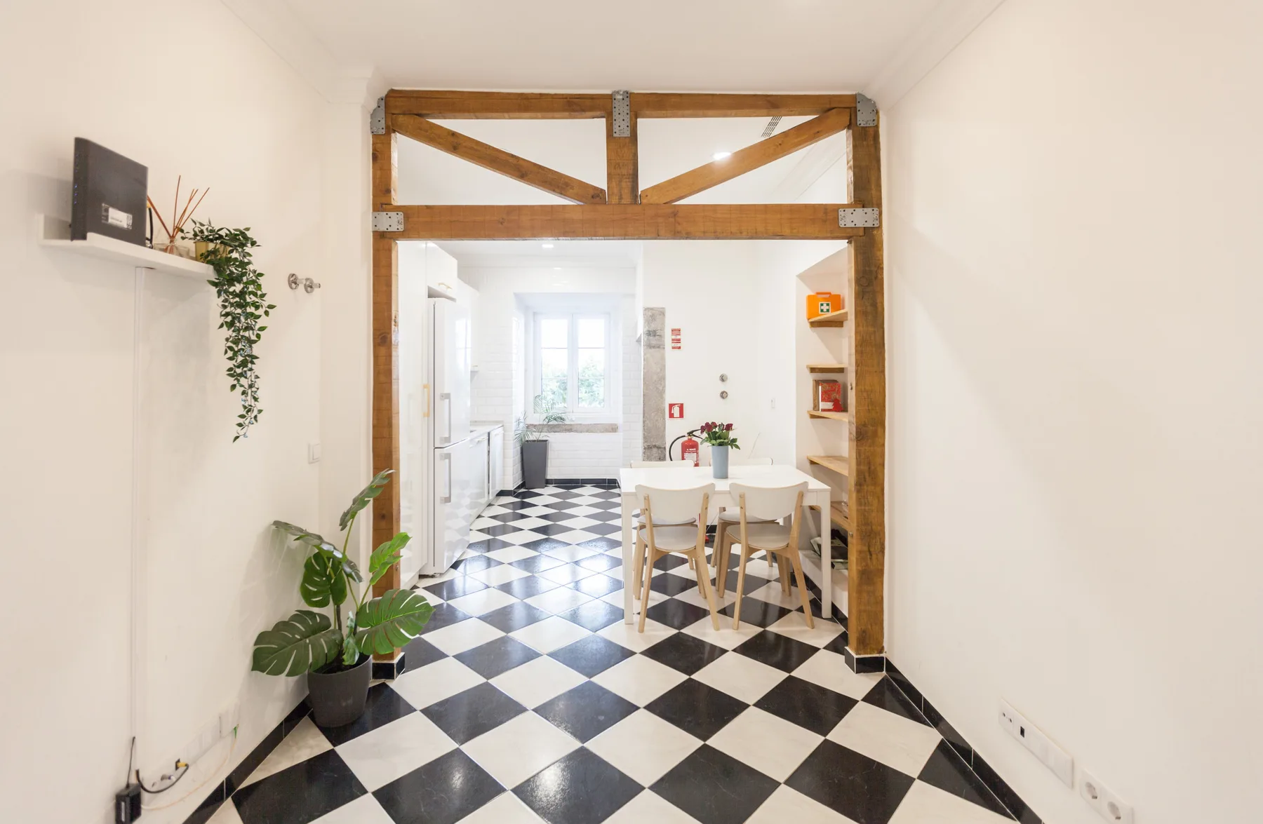A bright dining area with a table and chairs sits beyond a timber-framed opening.