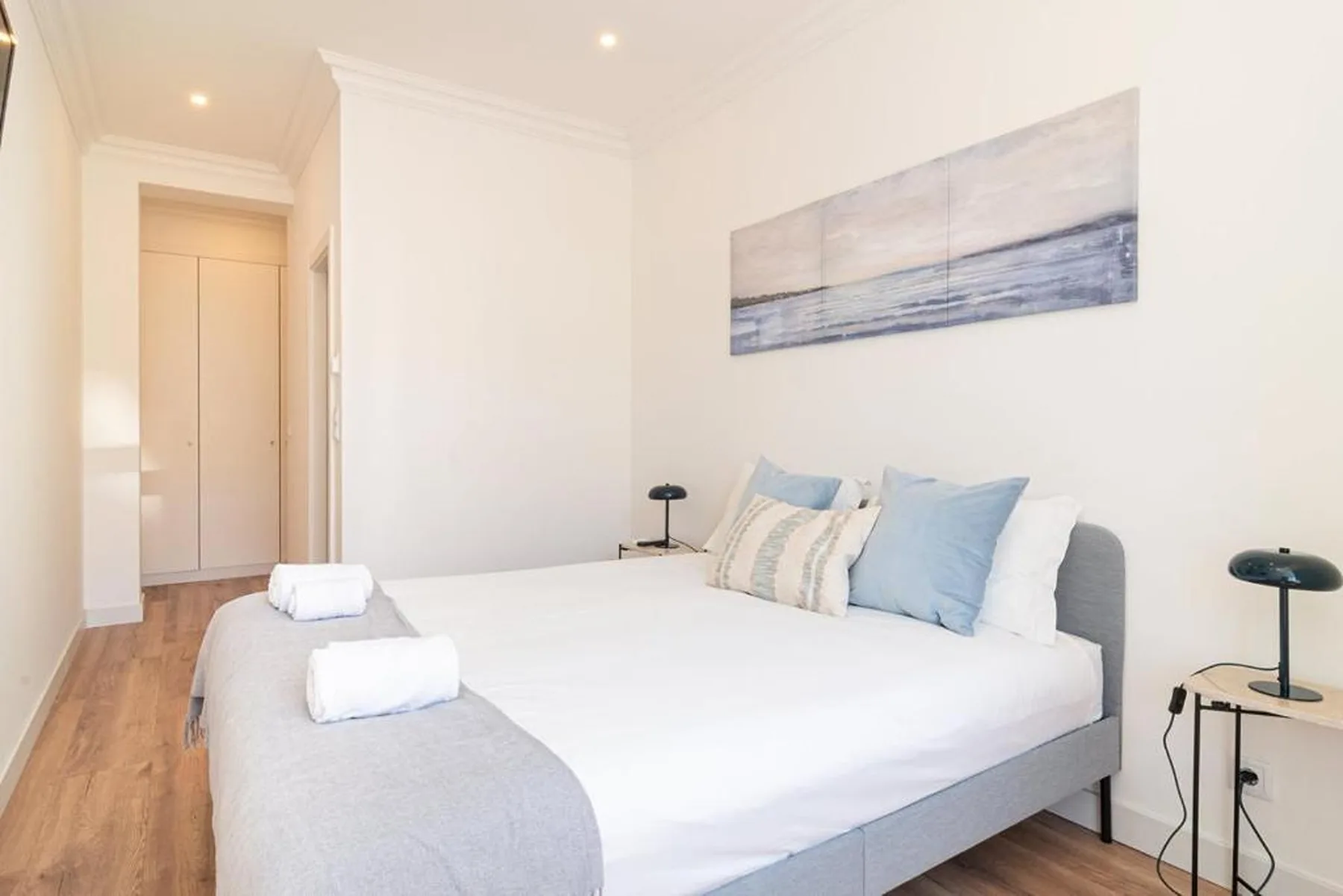 A bright bedroom with a neatly made bed and abstract wall art.