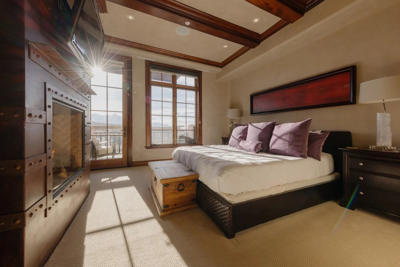 A bedroom with a large bed, wooden ceiling beams, and tall windows.