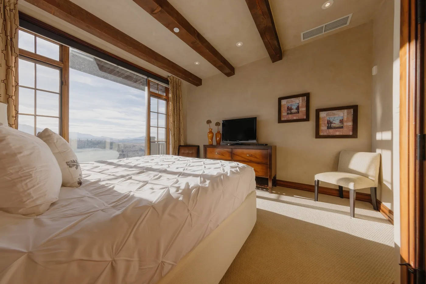 A bedroom with a large bed, television, and windows overlooking the landscape.