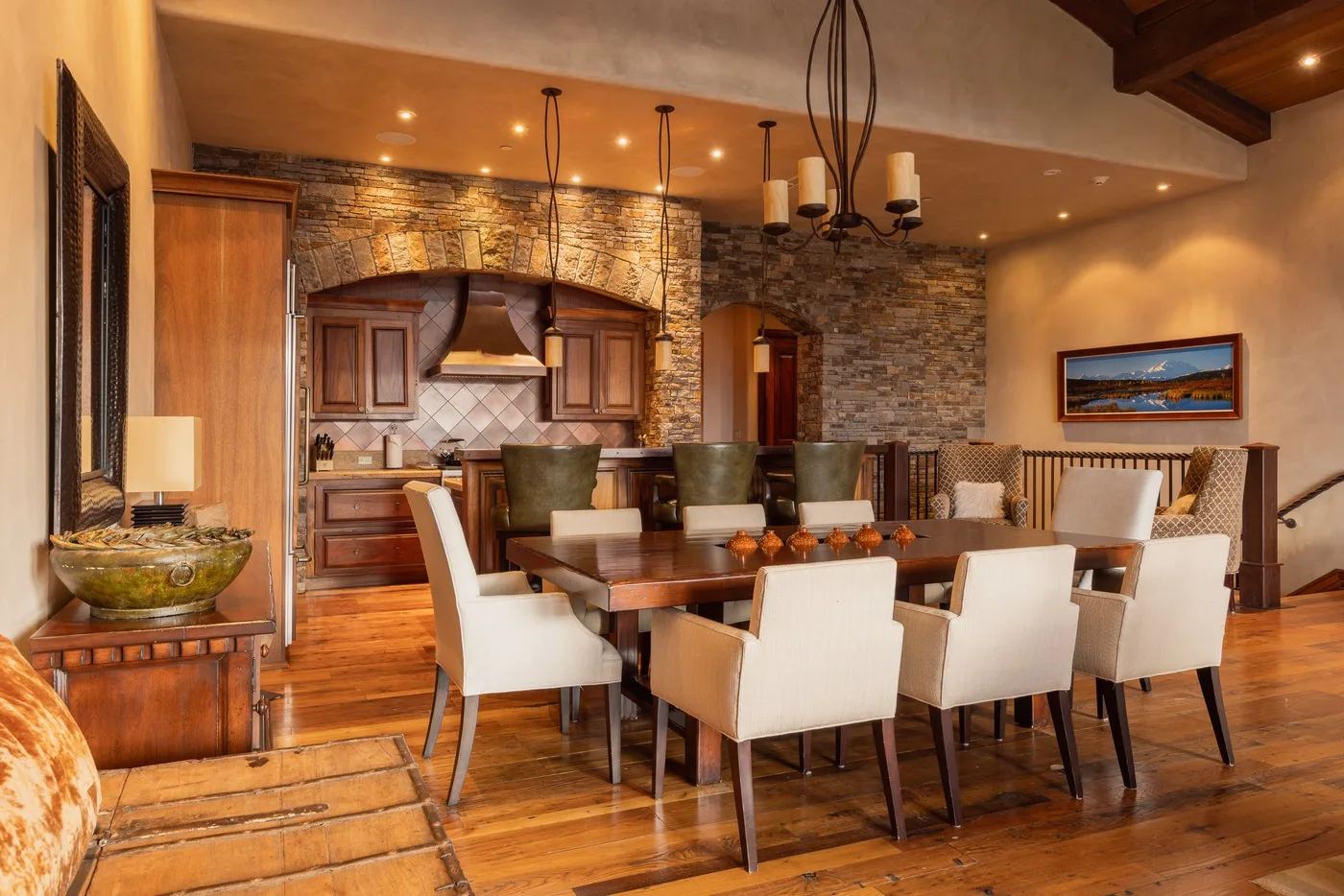 A dining area with a long table and cushioned seating beside a kitchen.