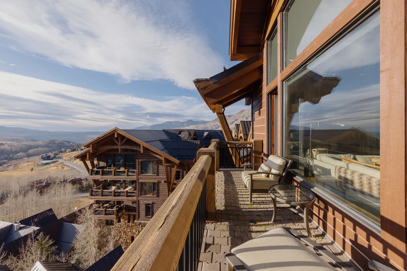 A balcony with outdoor seating overlooks a cluster of buildings and an open landscape.