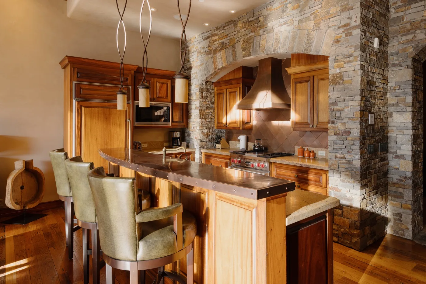 A kitchen with a wooden island, seating, and a stone-faced cooking area.