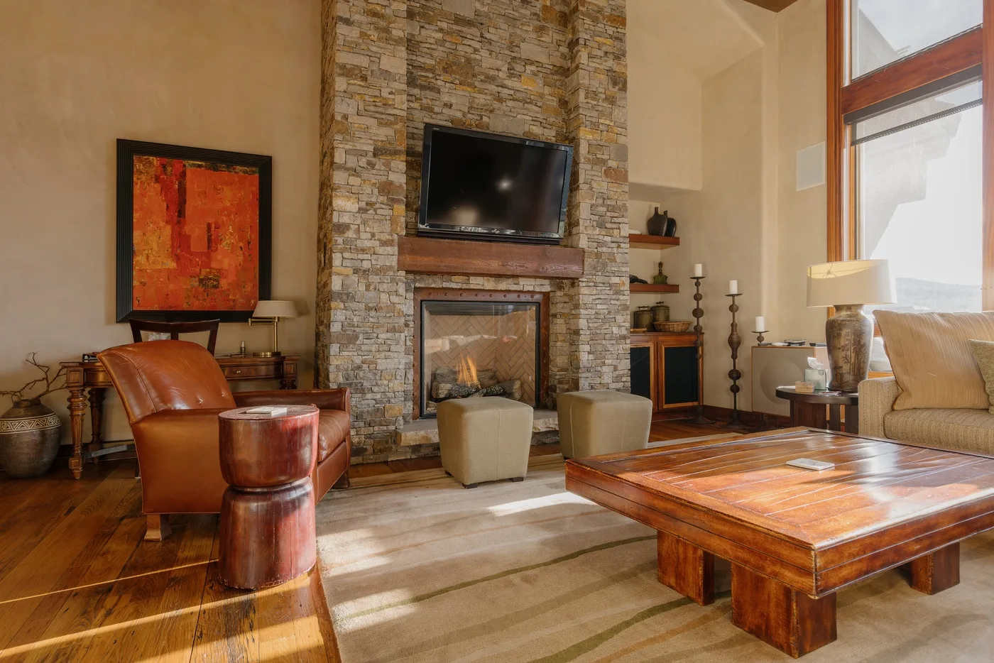 A living room with a stone fireplace, television, seating, and a wooden coffee table.