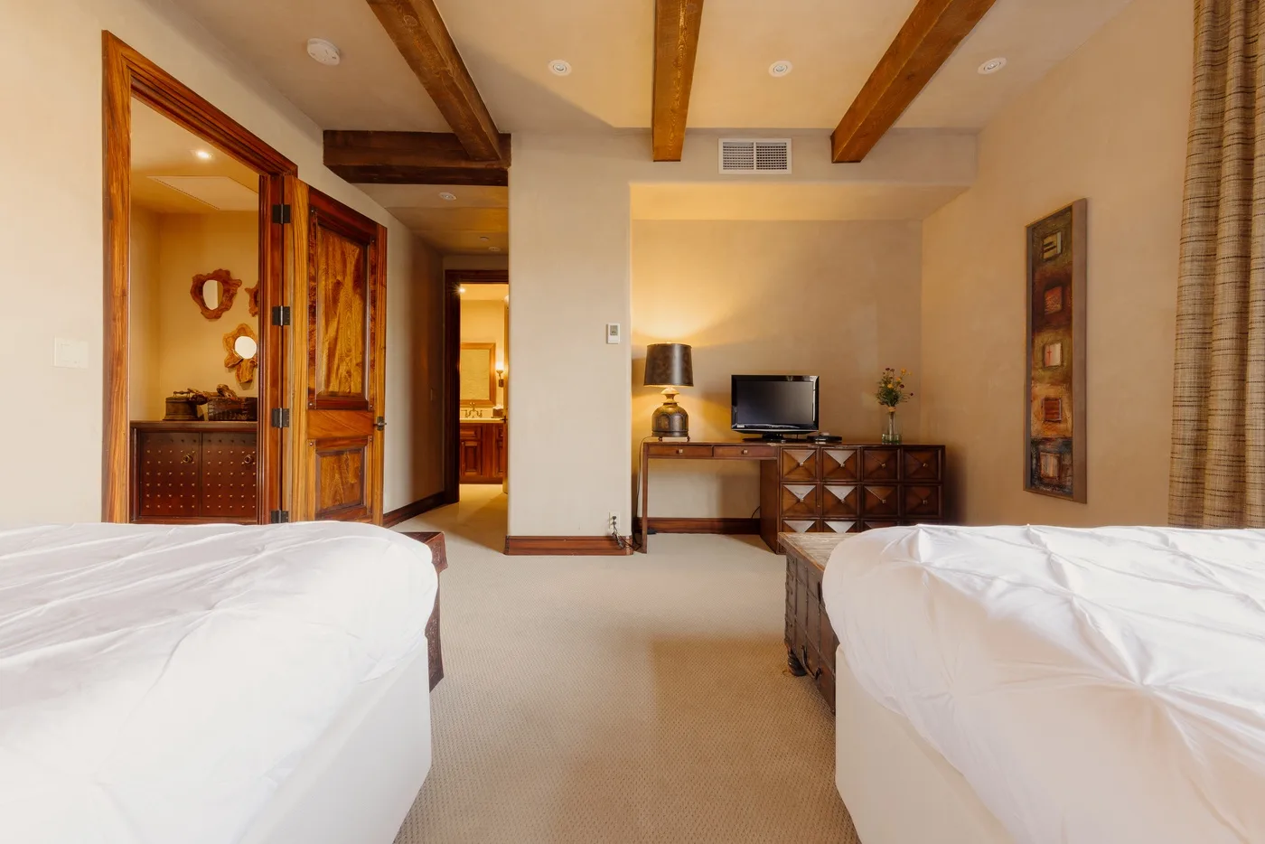 A bedroom with two beds, exposed wooden beams, and a television on a low cabinet.