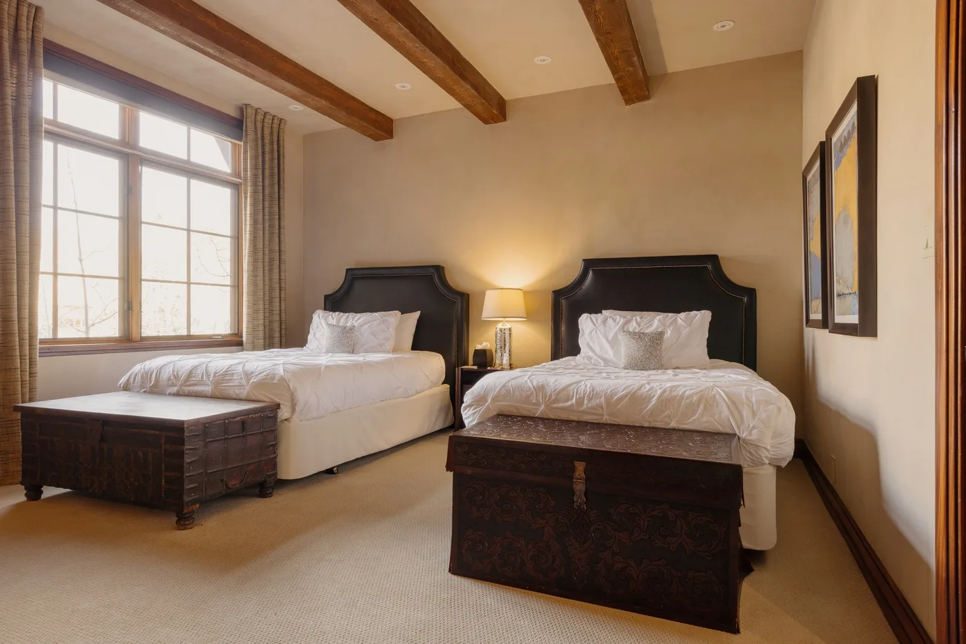 A bedroom with two beds, a bedside lamp, and a large window.
