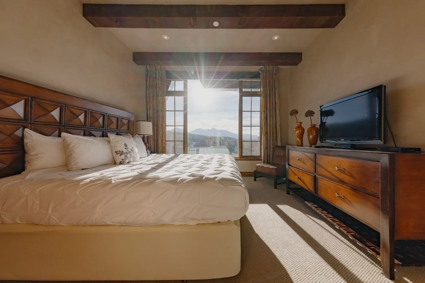 A bedroom with a large bed, a television, and a sunlit window.