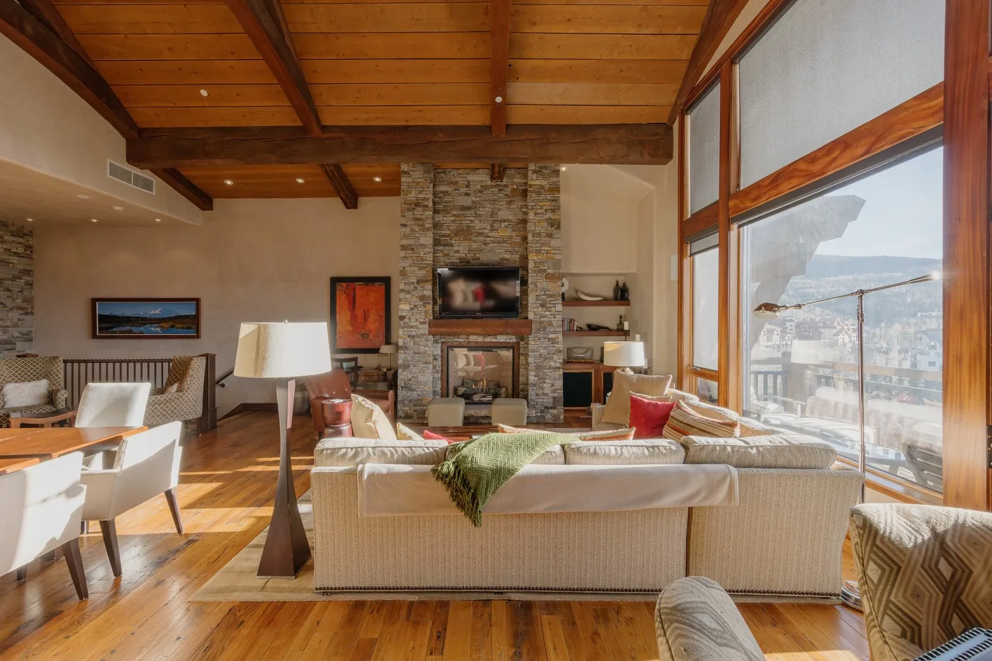 A bright living room with a stone fireplace, seating, and large windows.