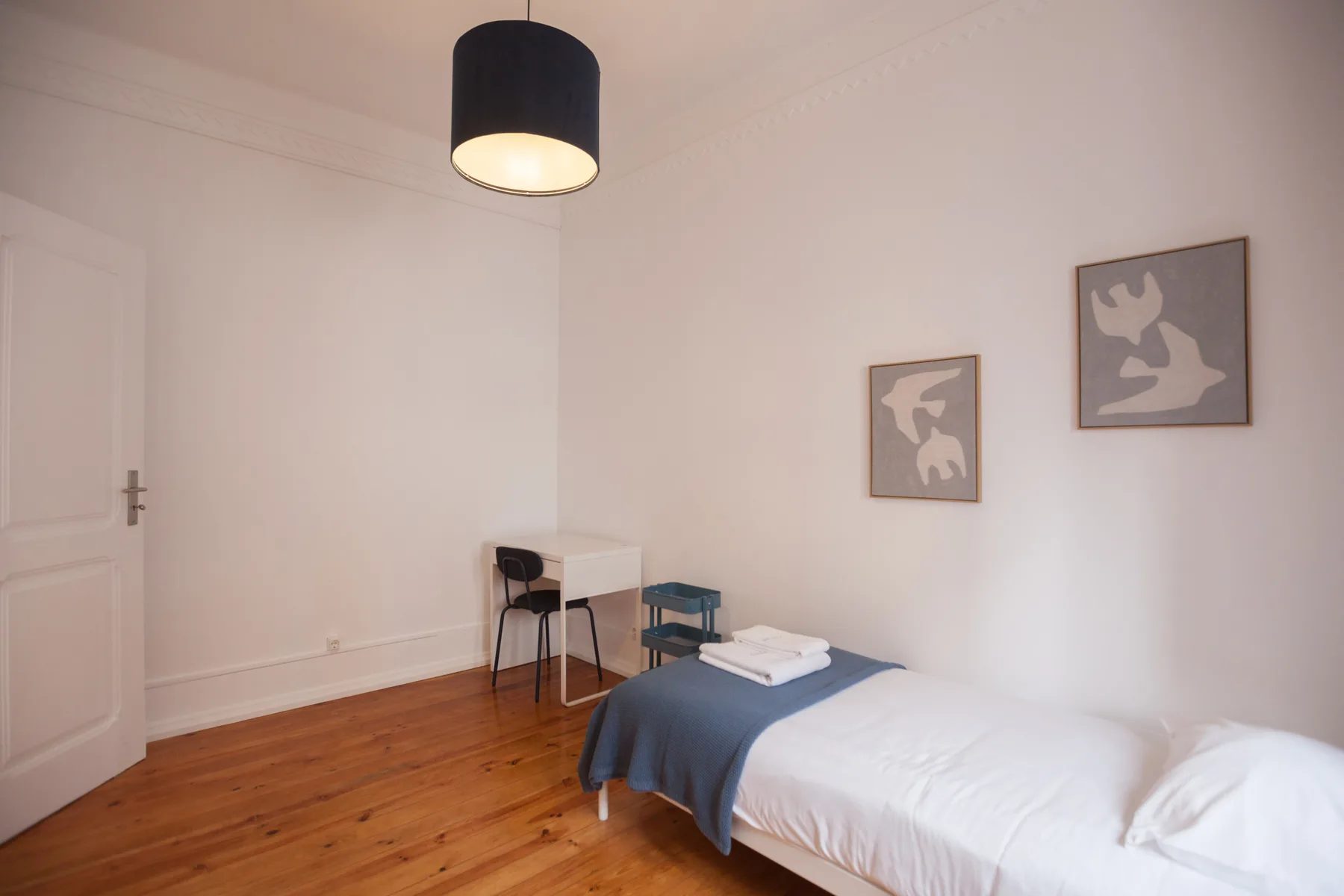 A bedroom with a single bed, a small desk, and framed artwork.