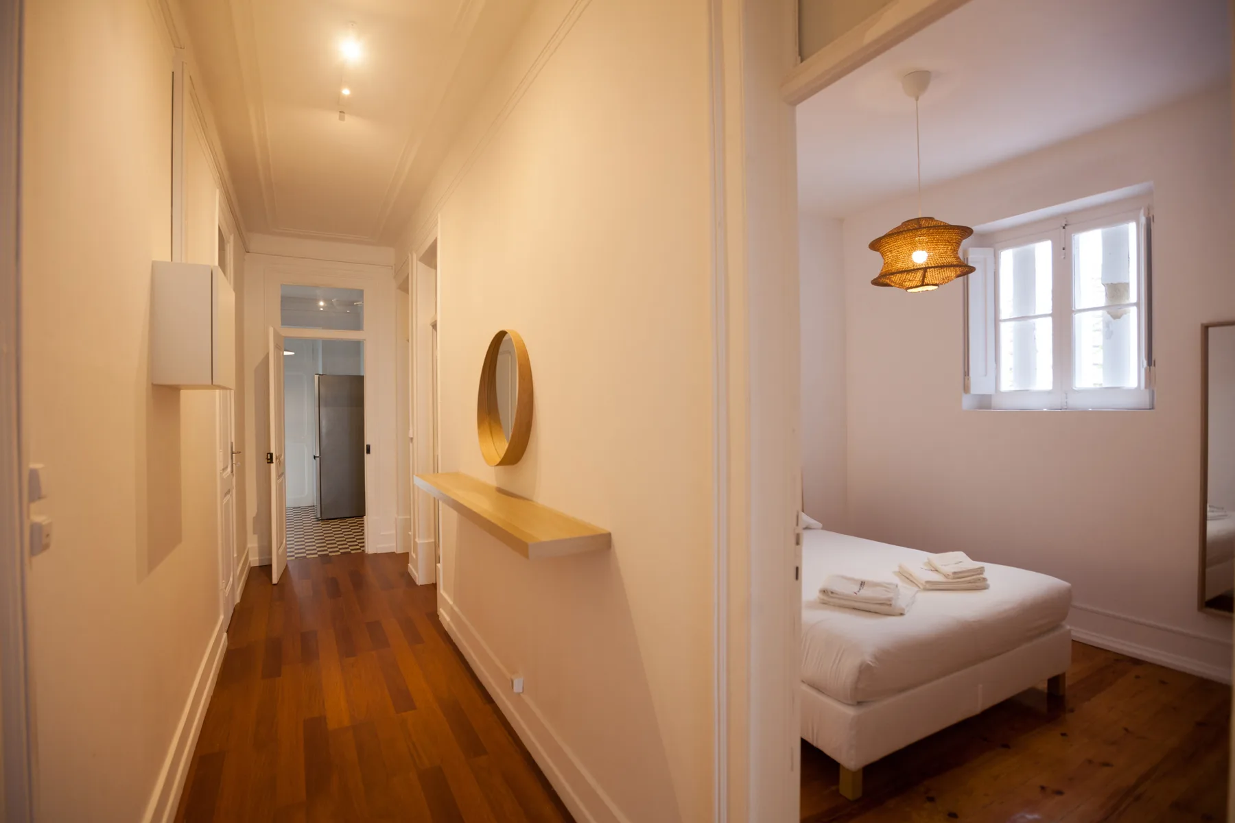 A hallway opens onto a bedroom with a bed beside a window.