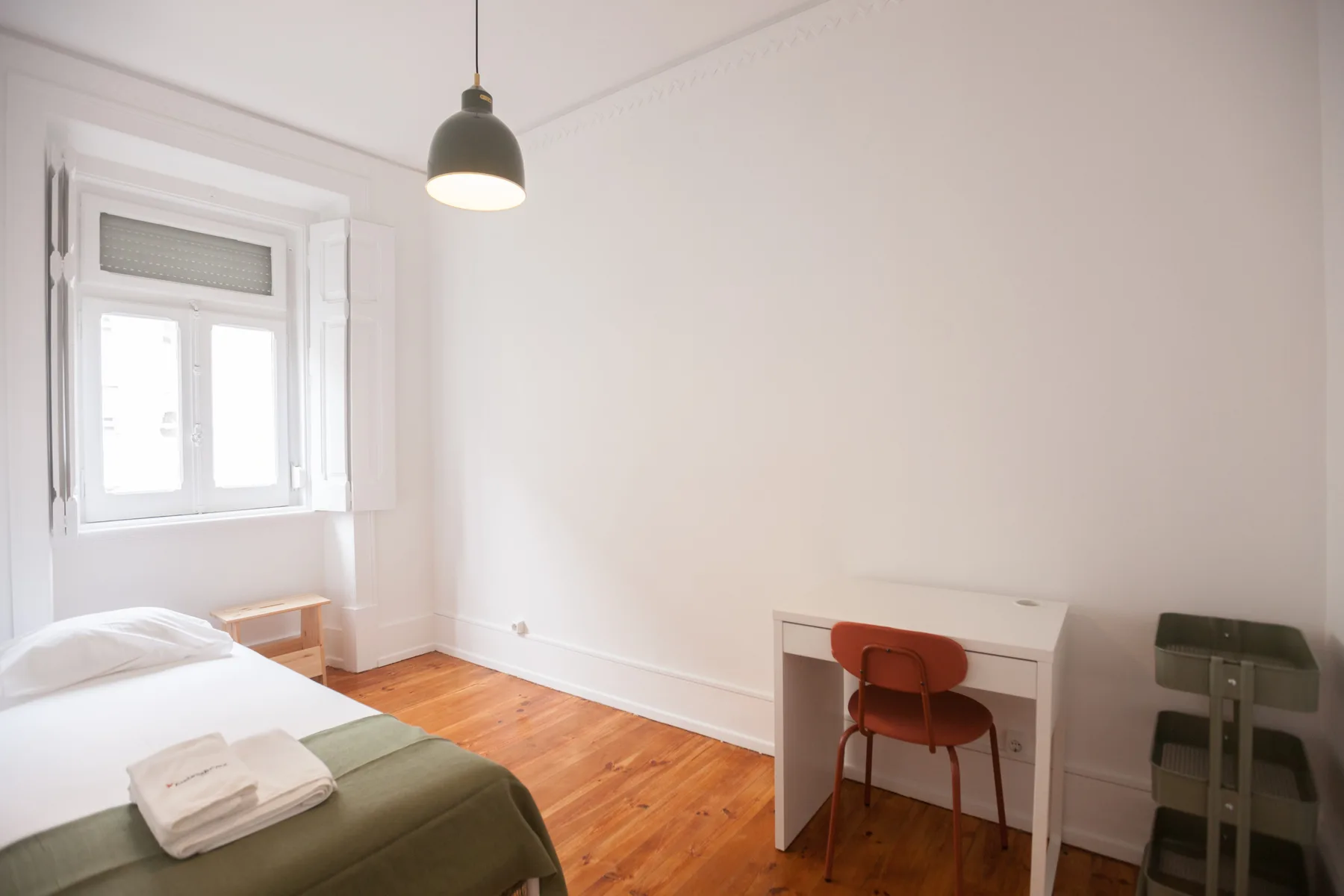 A bright bedroom with a bed, desk, and wooden floor.