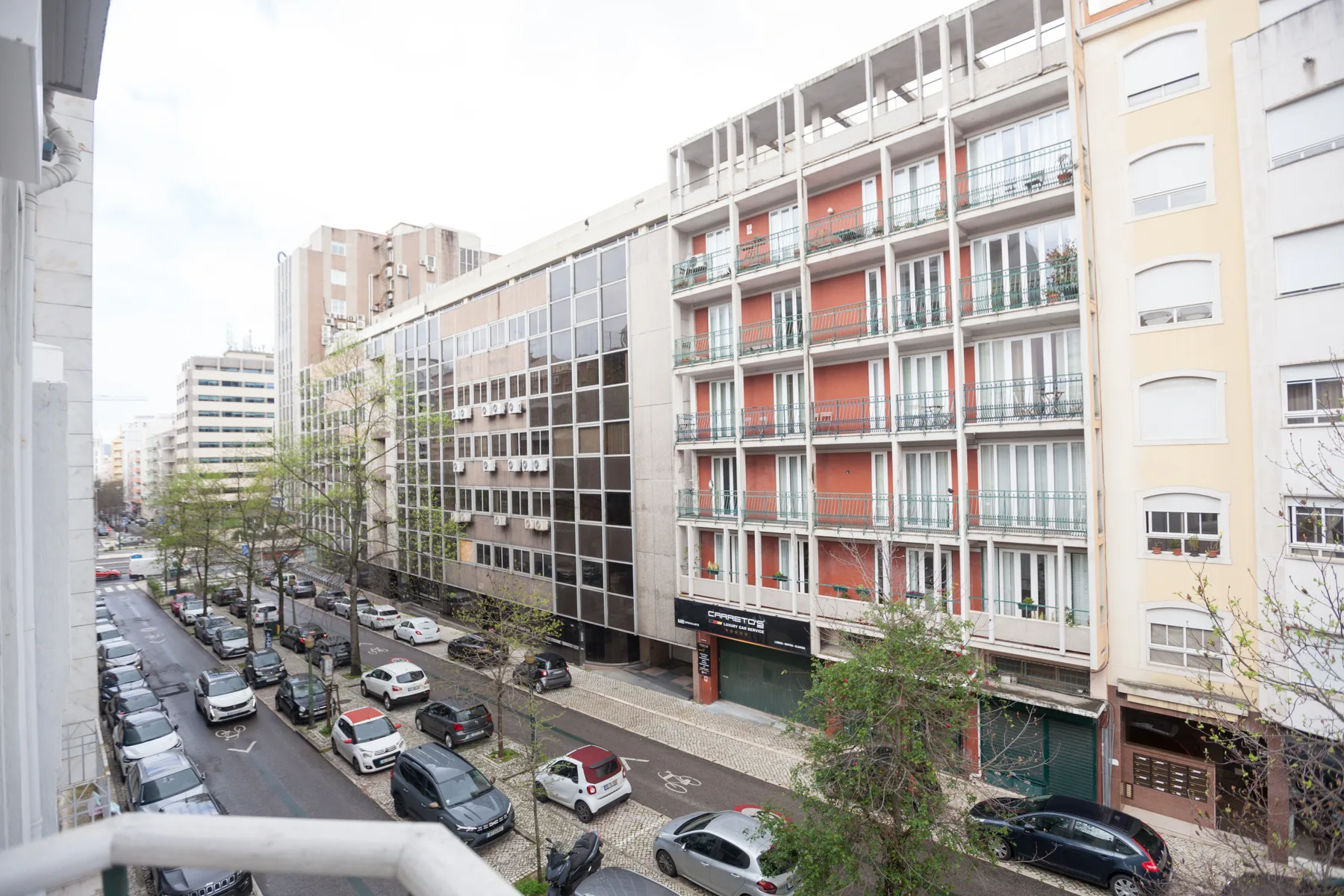 A city street with parked cars and apartment buildings lining both sides.