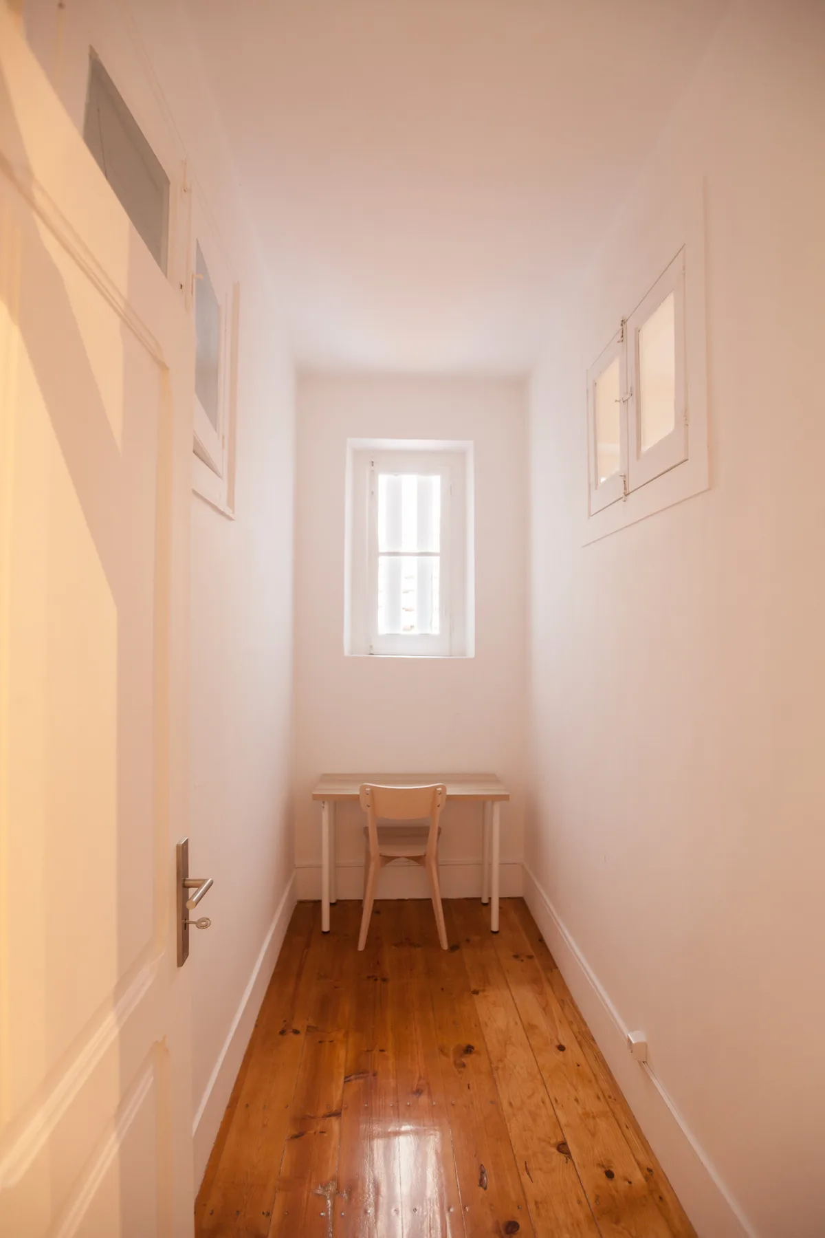 A narrow hallway with a small desk and chair beneath a window.