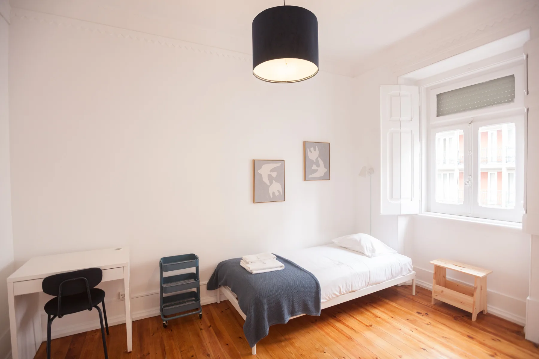 A bright bedroom with a bed, desk, and window.