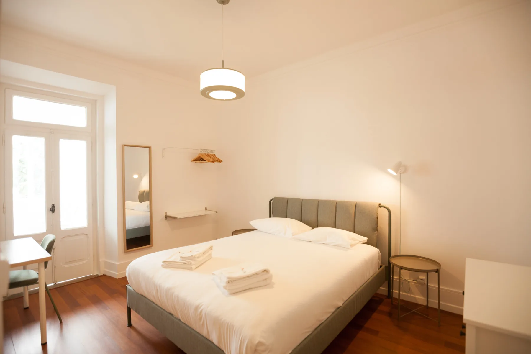 A bedroom with a neatly made bed, bedside tables, and a tall window.