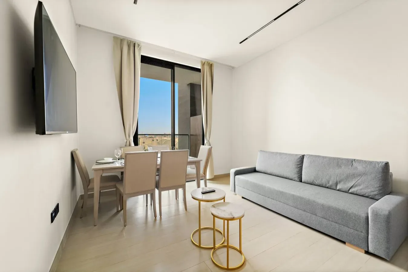 A bright living room with a gray sofa, dining table, and large window.