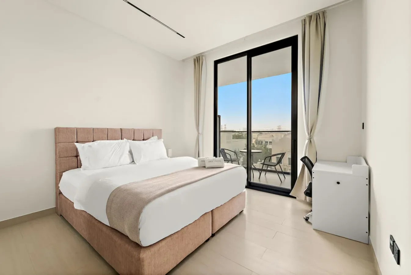 A bright bedroom with a large bed beside glass doors opening to a balcony.