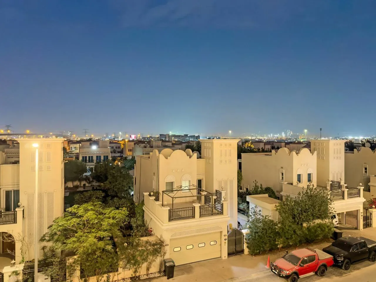 A nighttime cityscape shows illuminated buildings beyond residential rooftops and trees.