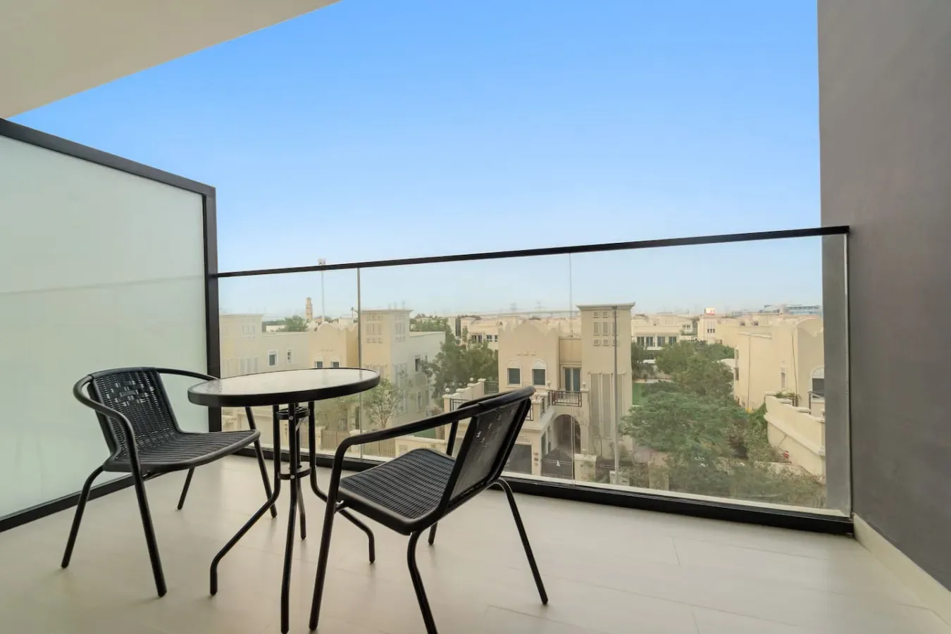A balcony seating area with a small table overlooks nearby buildings and trees.
