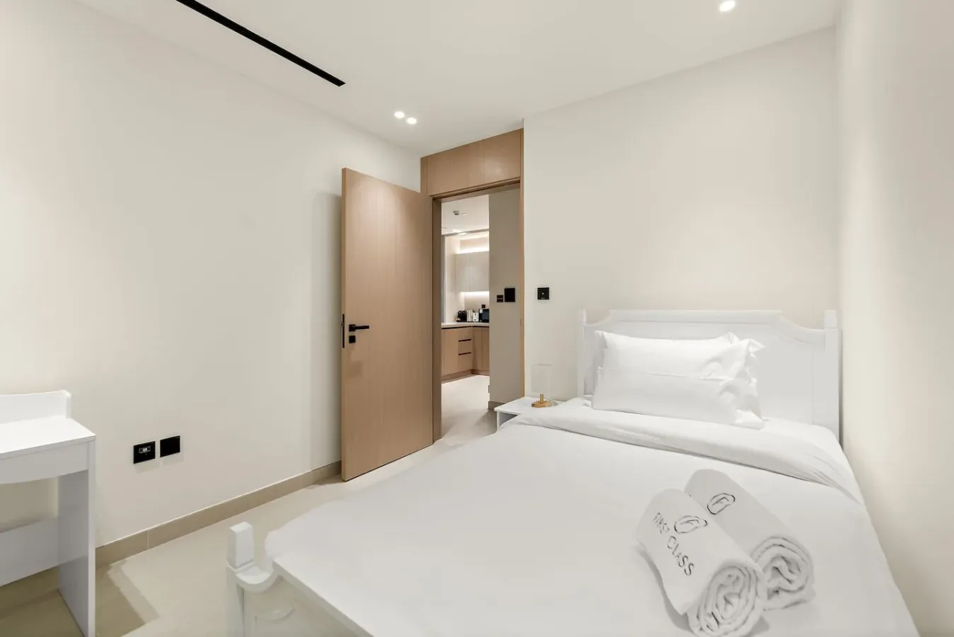 A bright bedroom with a white bed and an open doorway.