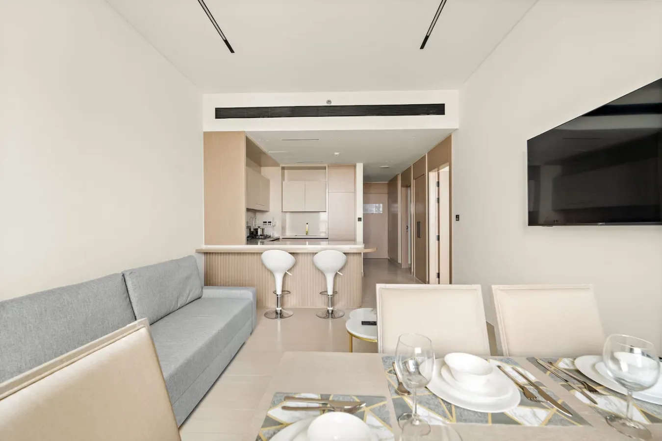 A bright living and dining area opens onto a compact kitchen, with seating and a wall-mounted television.