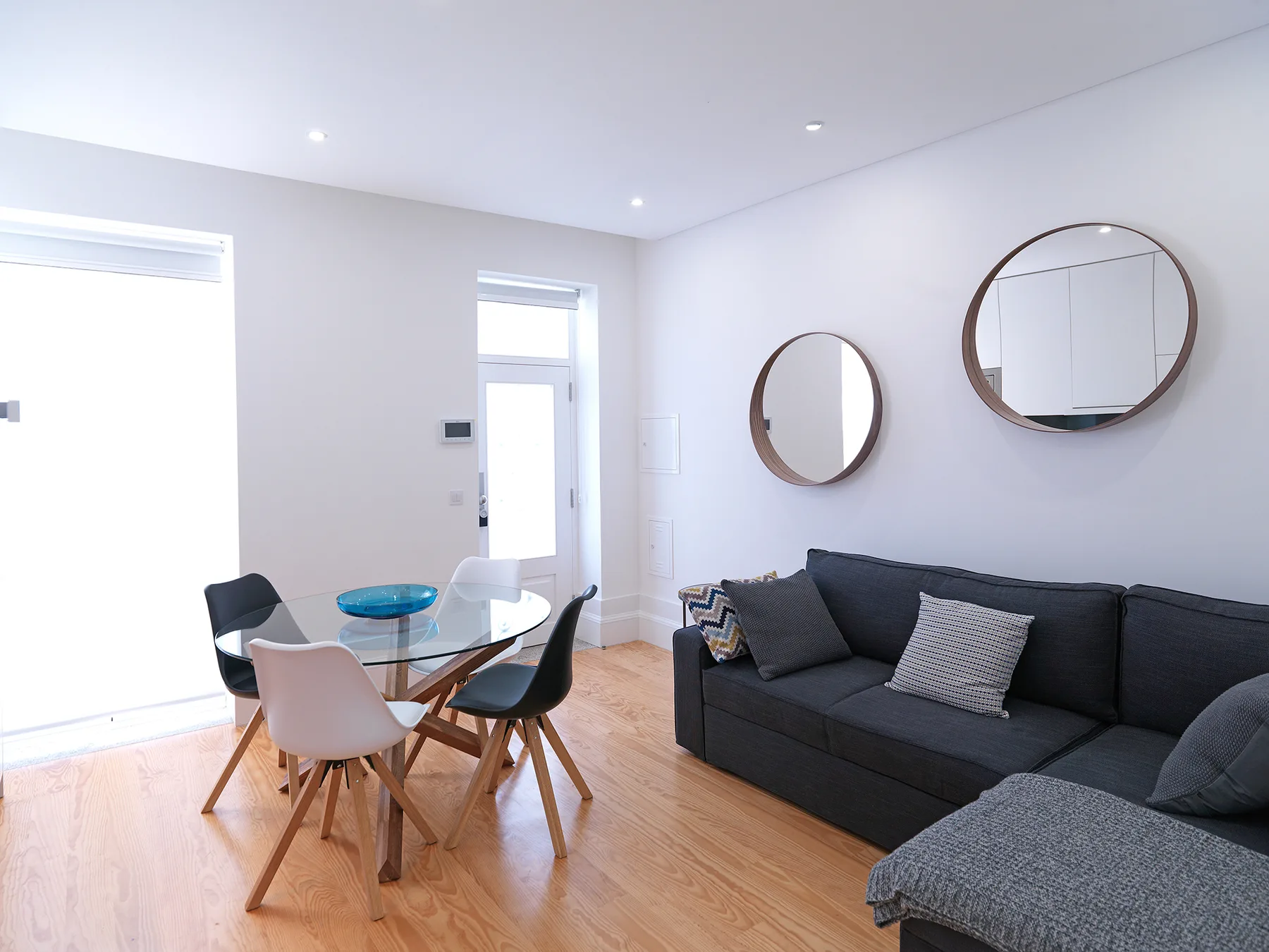 Una sala luminosa con un sofá oscuro y una mesa de comedor de vidrio.