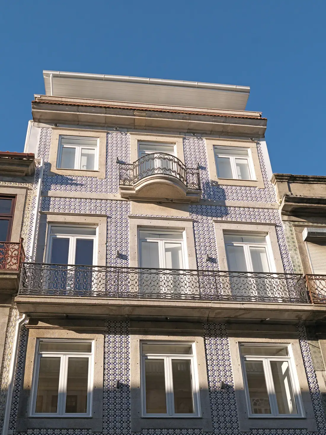Una fachada de azulejos con varias ventanas y balcones de hierro forjado bajo un cielo azul.