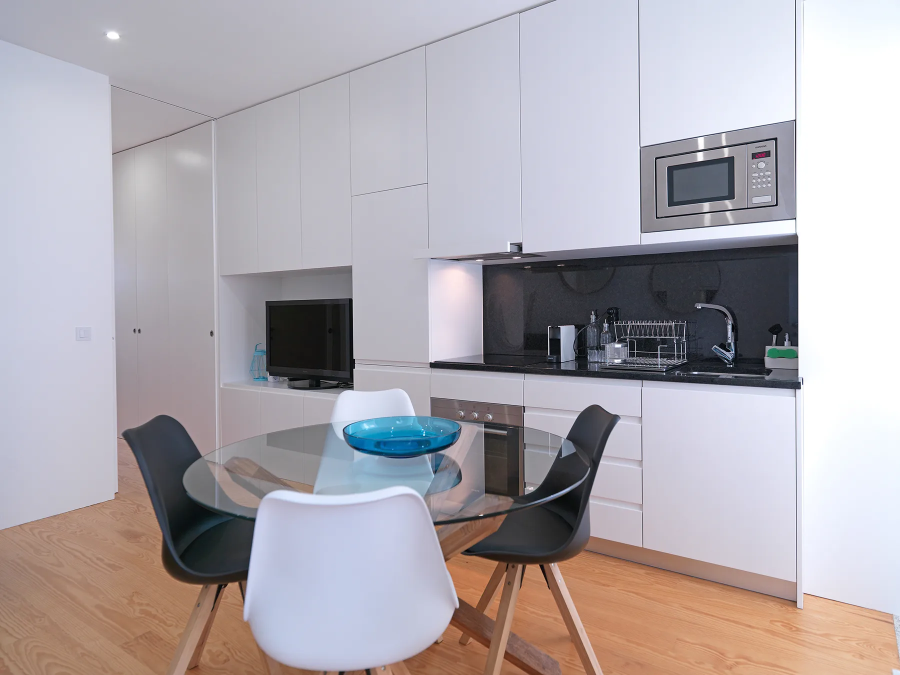 A modern kitchen and dining area with a glass table and dark backsplash.
