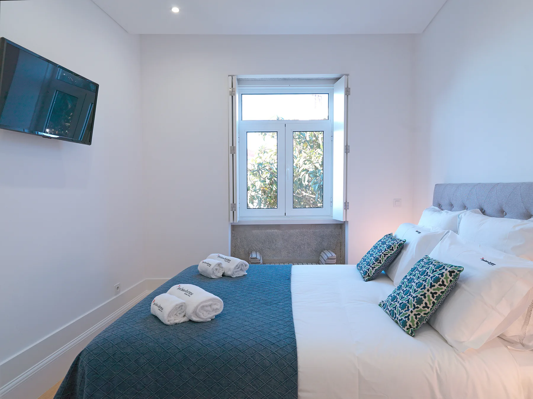 Un dormitorio luminoso con una cama grande y una ventana con vistas a árboles frondosos.