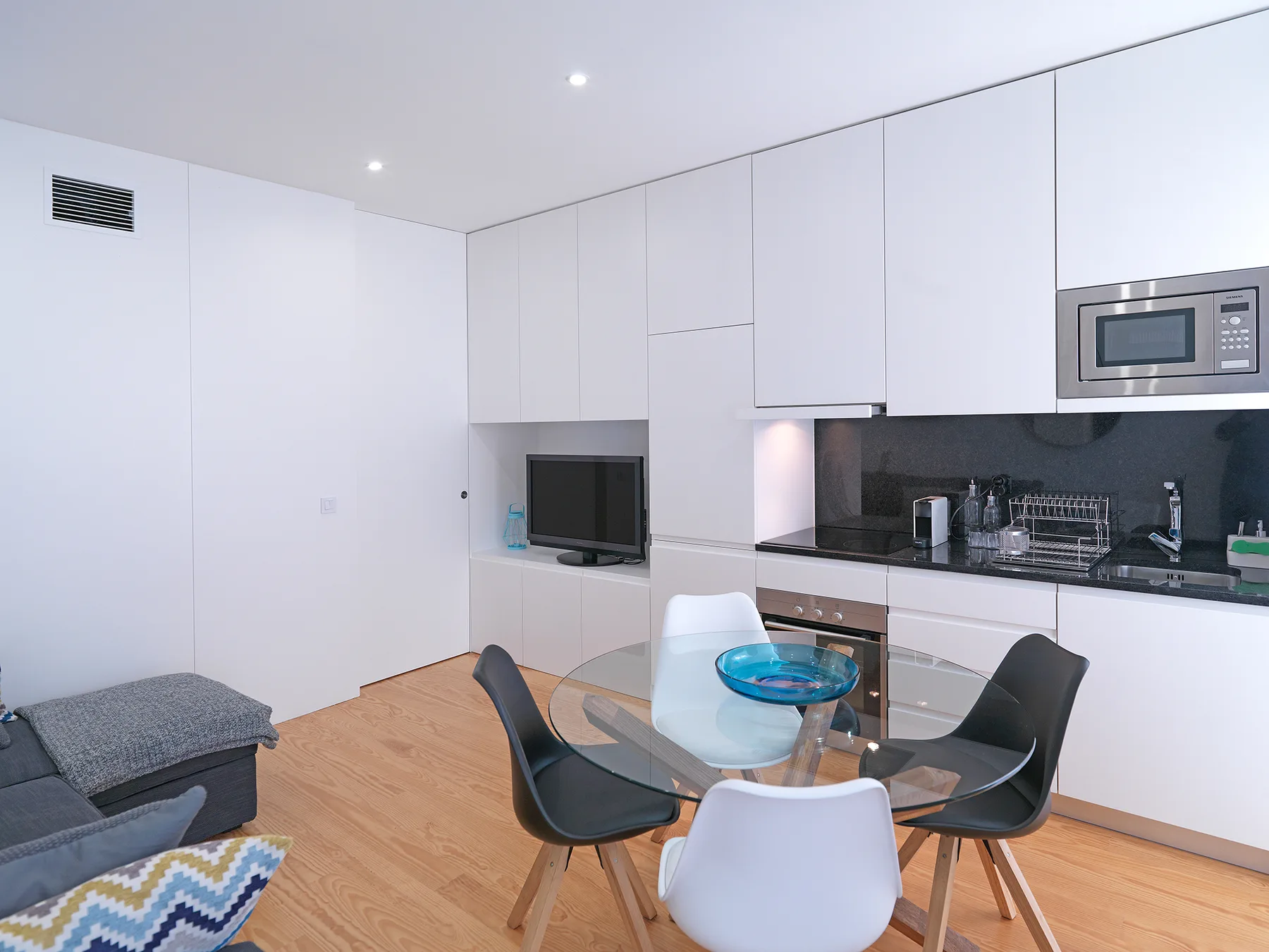 A modern kitchen and dining area with a glass table and dark cabinetry.