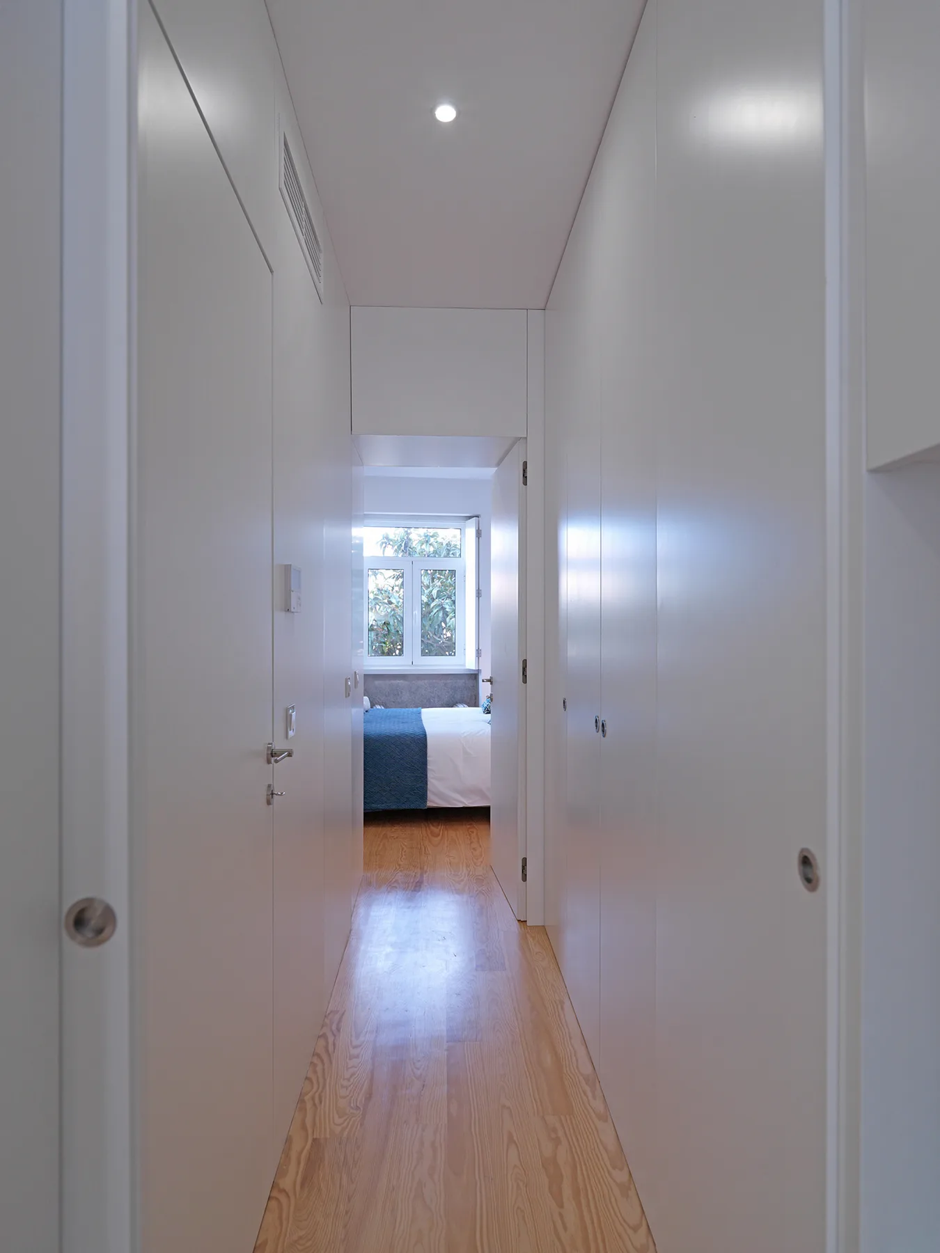Un pasillo estrecho con suelo de madera clara conduce a un dormitorio.