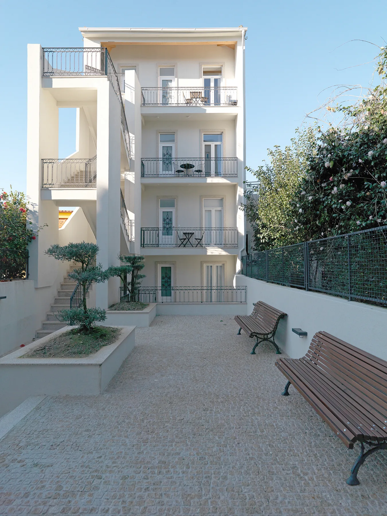 Un edificio de apartamentos de varias plantas da a un patio pavimentado con bancos y zonas ajardinadas.