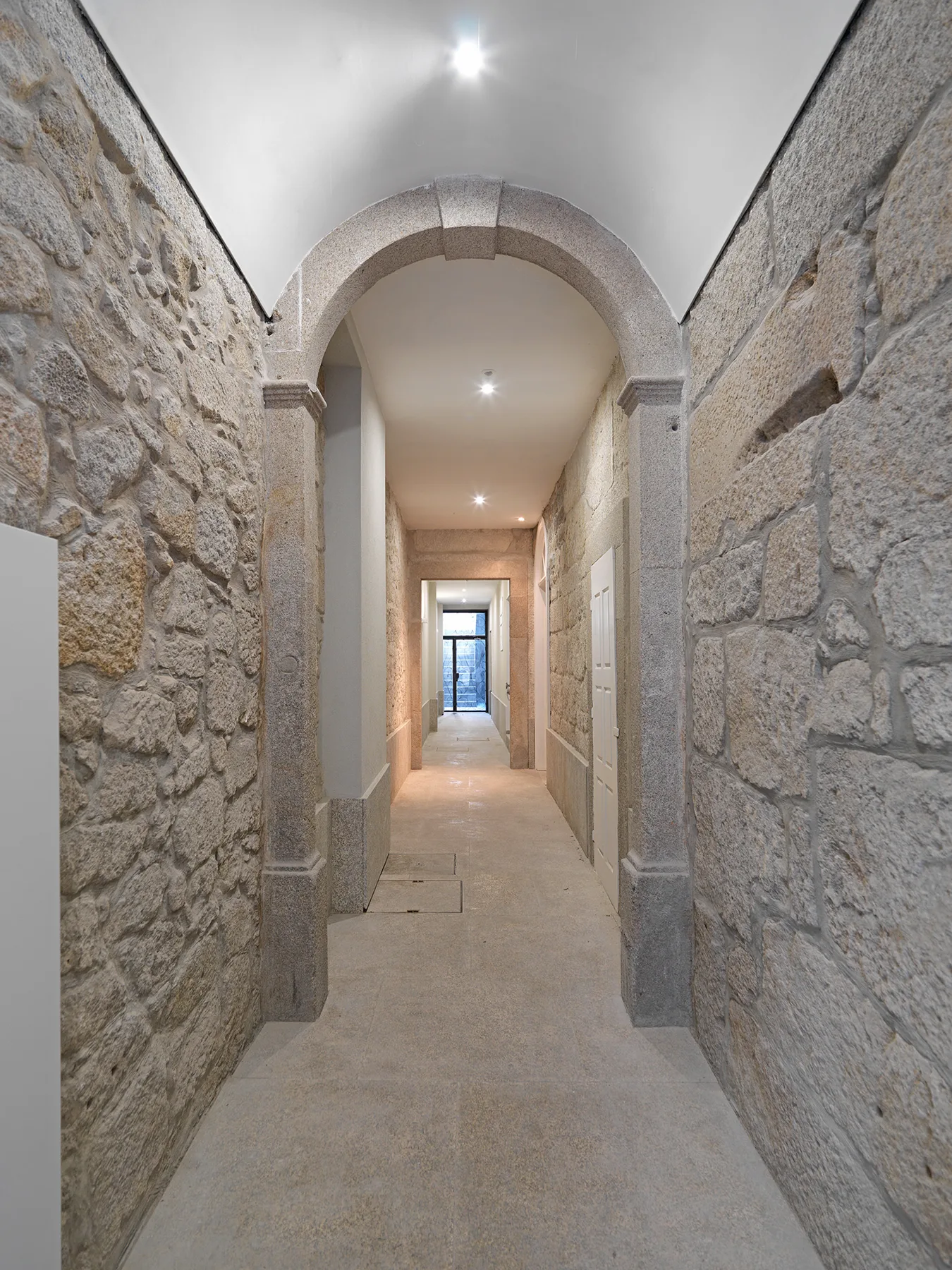 Un pasillo de piedra con arcos y una vista hacia una ventana.