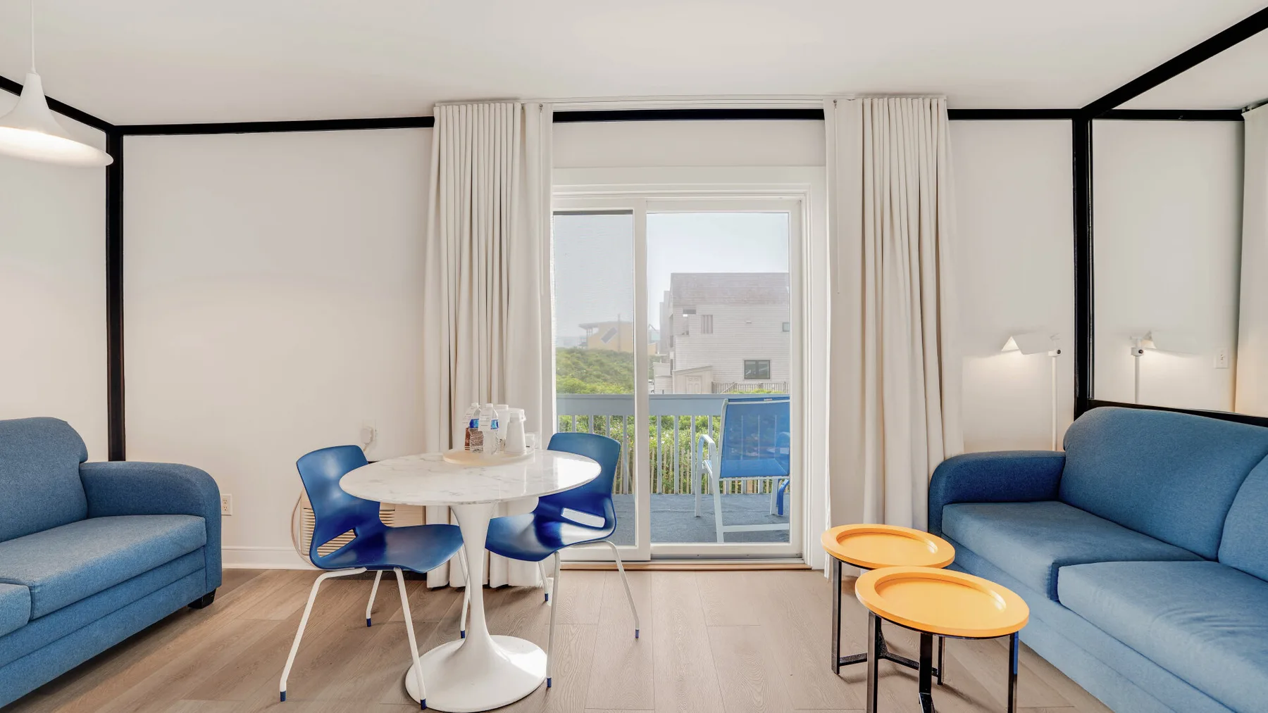 Una sala de estar con asientos azules, una mesa pequeña y puertas de cristal que dan a un balcón.